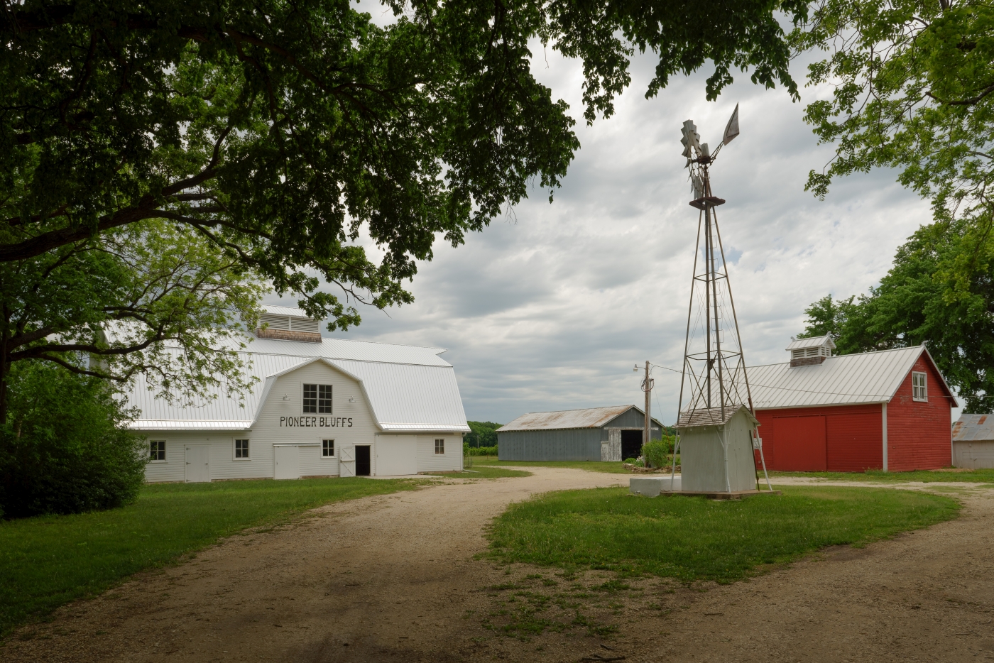 View of windmill with trees, main barn and curving driveway